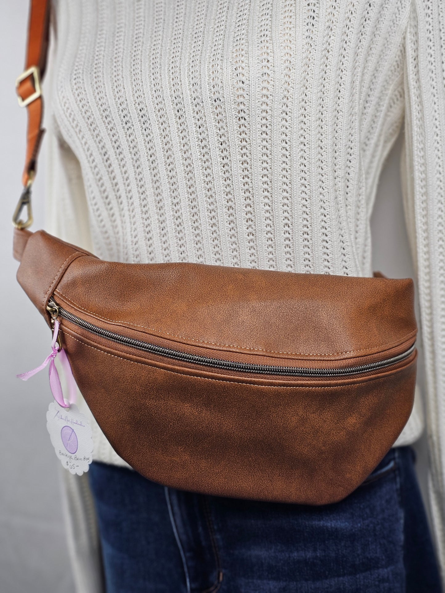 Brown faux leather pouch bag with mushroom cotton interior fabric and one zippered interior pocket and one slip pocket. Antique brass hardware and brown nylon one inch strap.