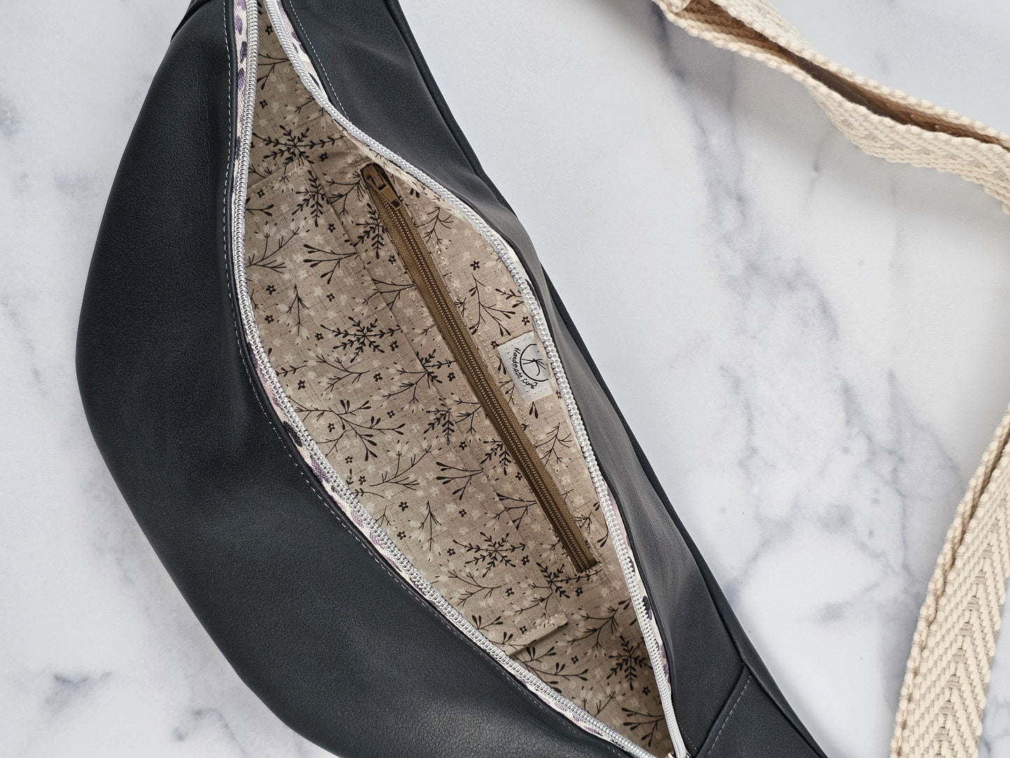 Dark gray faux leather sling fanny pack with gray leopard print zipper and light gray chevron strap. Interior gray floral with interior zip and slip pockets.