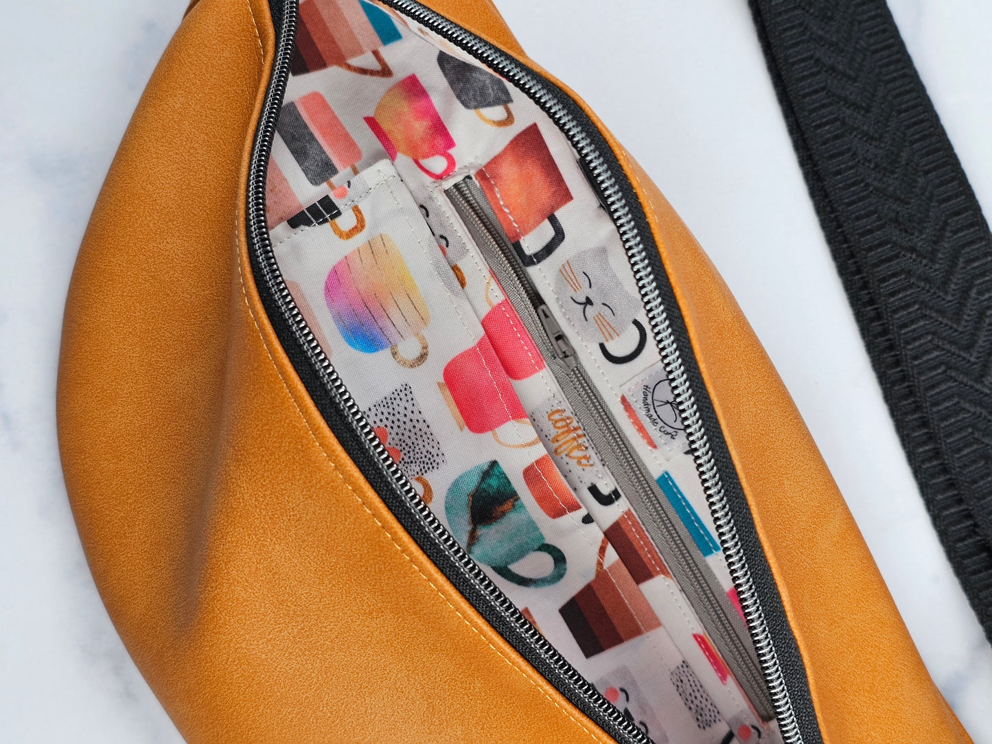 Tan faux leather bum bag, sling bag with fun cat ug cotton lining, black textured strap, with interior zippered and slip pockets.