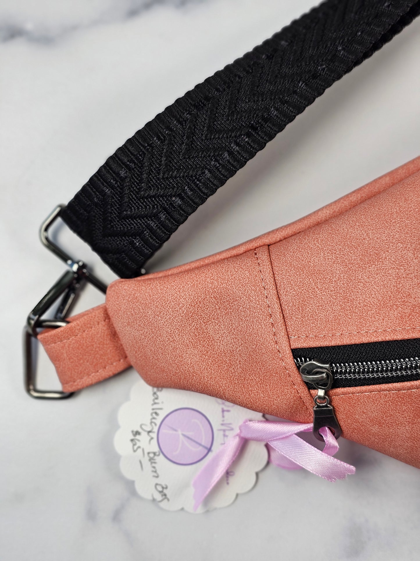 Pink bag with black strap and visible brand tag on a marble background