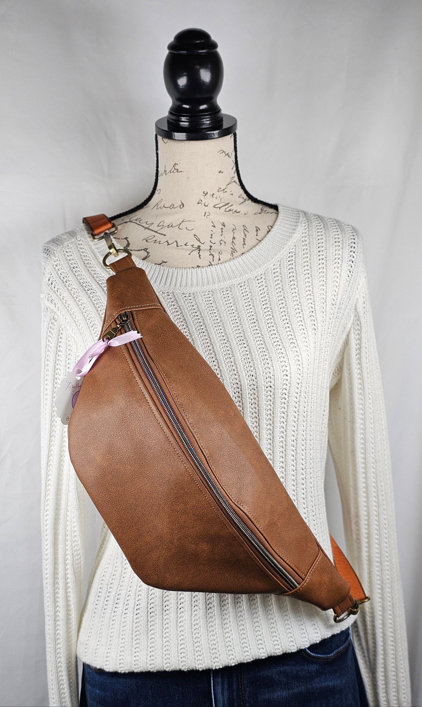 Brown faux leather waist bag, sling style bag, fanny pack, with mushroom cotton interior fabric with one interior zippered pocket and one interior slip pocket and antique brass hardware.