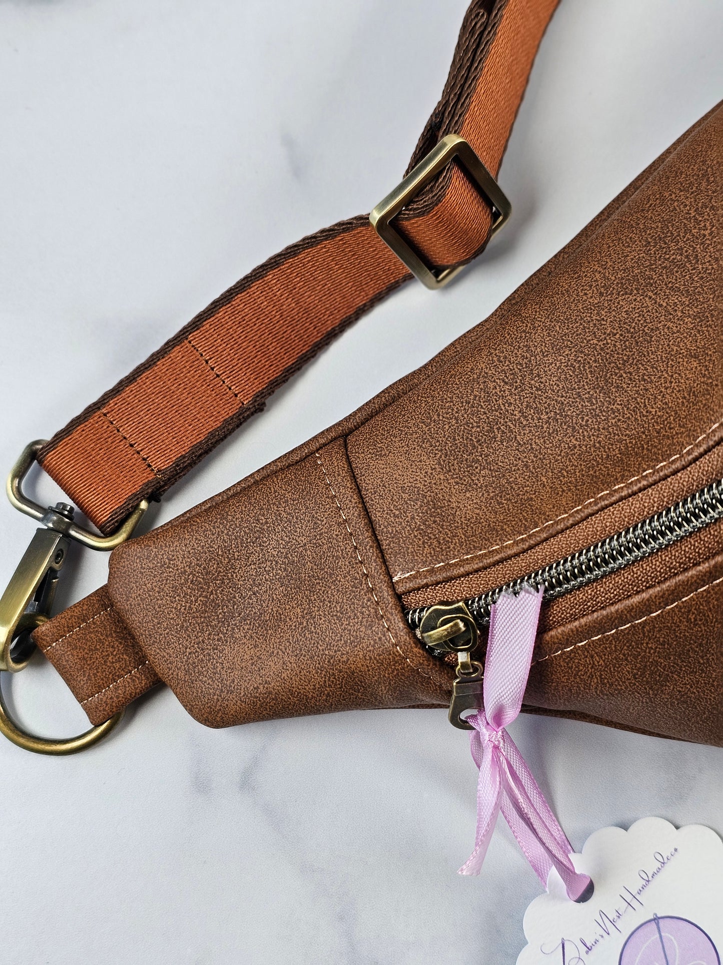 Brown faux leather pouch bag with mushroom cotton interior fabric and one zippered interior pocket and one slip pocket. Antique brass hardware