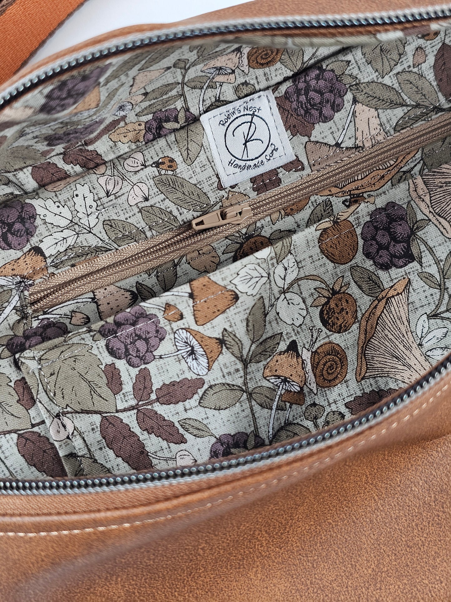 Brown faux leather pouch bag with mushroom cotton interior fabric and one zippered interior pocket and one slip pocket. Antique brass hardware