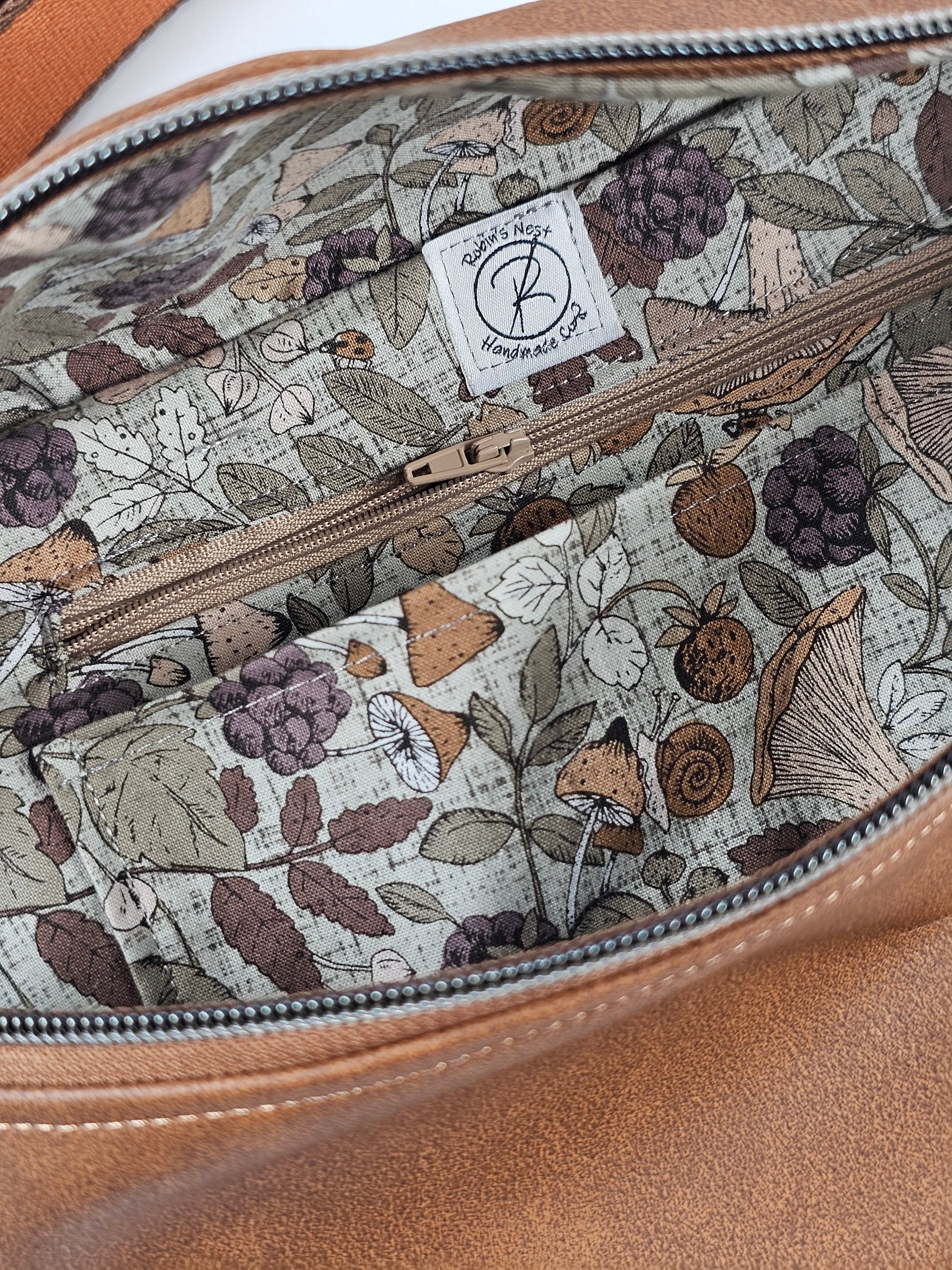 Brown faux leather pouch bag with mushroom cotton interior fabric and one zippered interior pocket and one slip pocket. Antique brass hardware