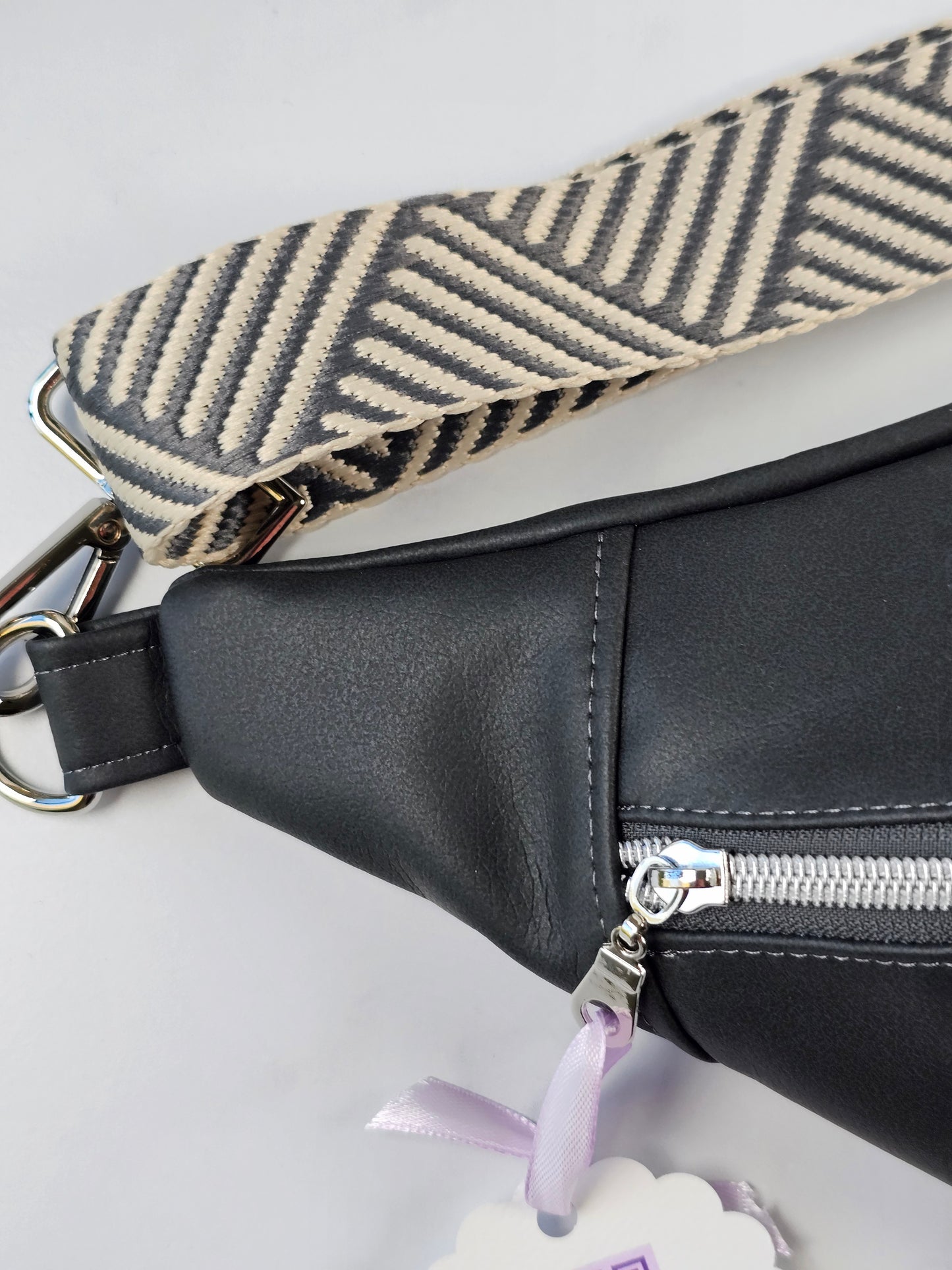 Dark gray sling bag fanny pack with a patterned strap on a light gray background