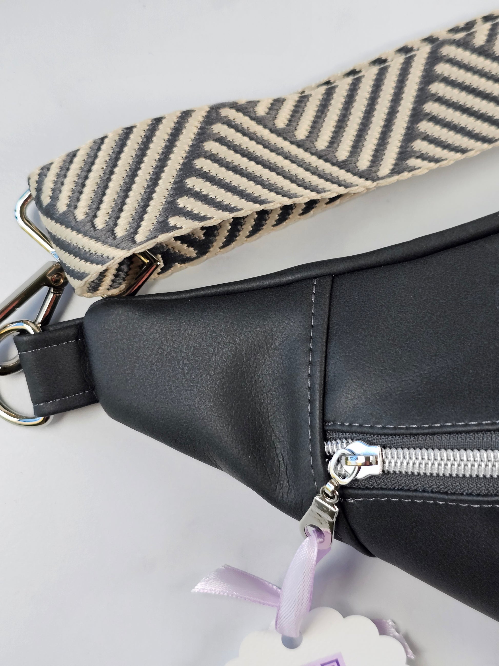 Dark gray sling bag fanny pack with a patterned strap on a light gray background