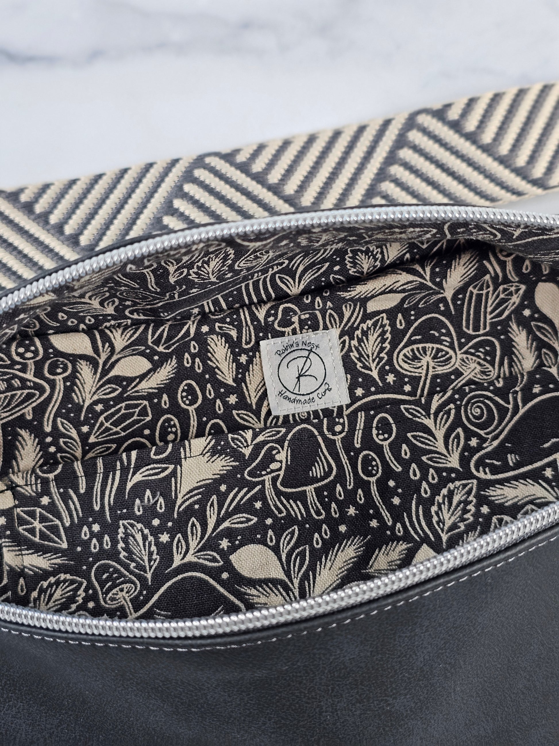 Dark gray sling bag with a gray and beige strap and a gray mushroom cotton canvas interior with a slip pocket. Silver hardware.