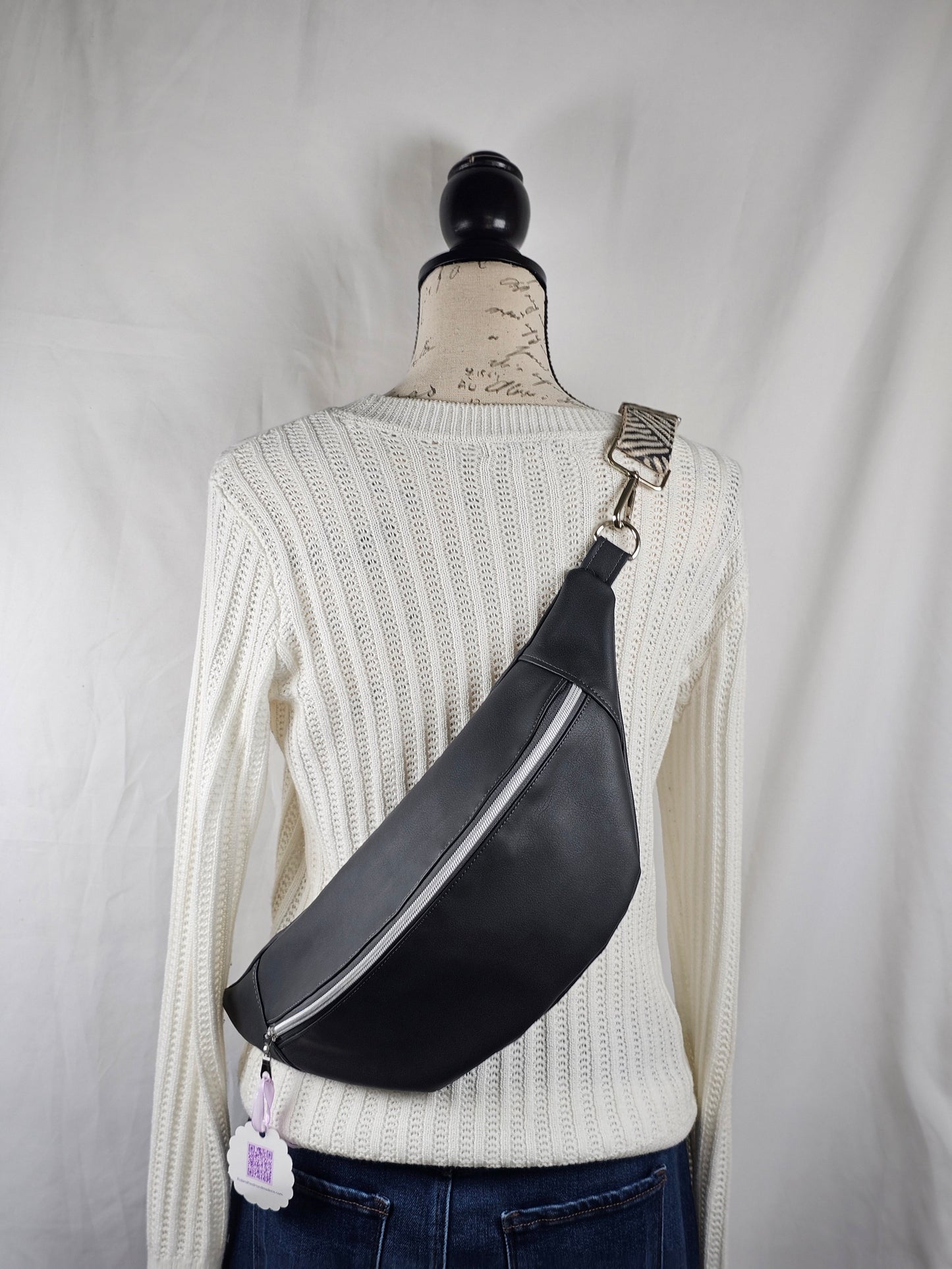 Dark gray sling bag with gray and white stiped strap, silver hardware, gray mushroom cotton canvas interior fabric with one slip pocket.