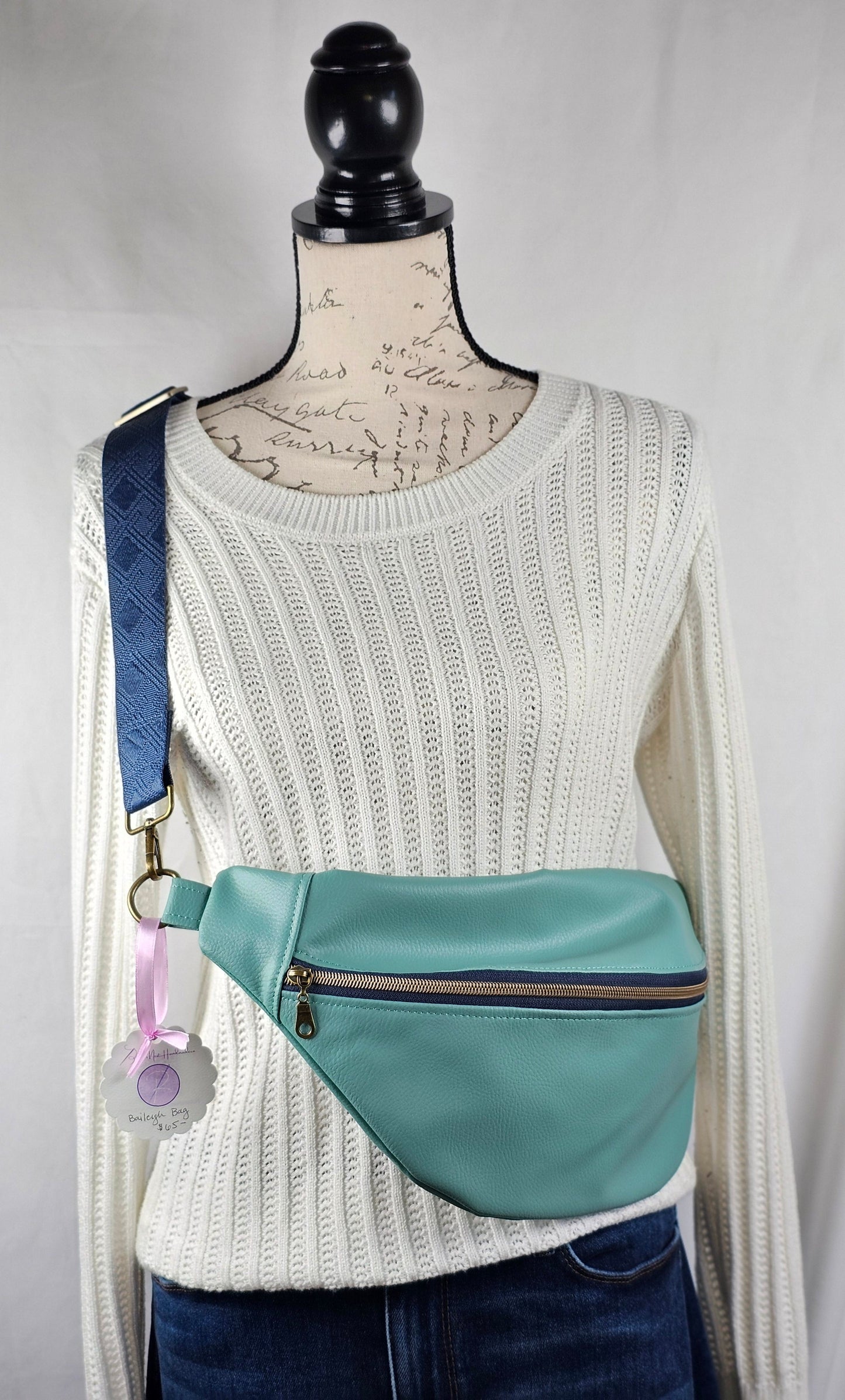 Mannequin wearing a white sweater with a green pouch and blue accents on a plain background