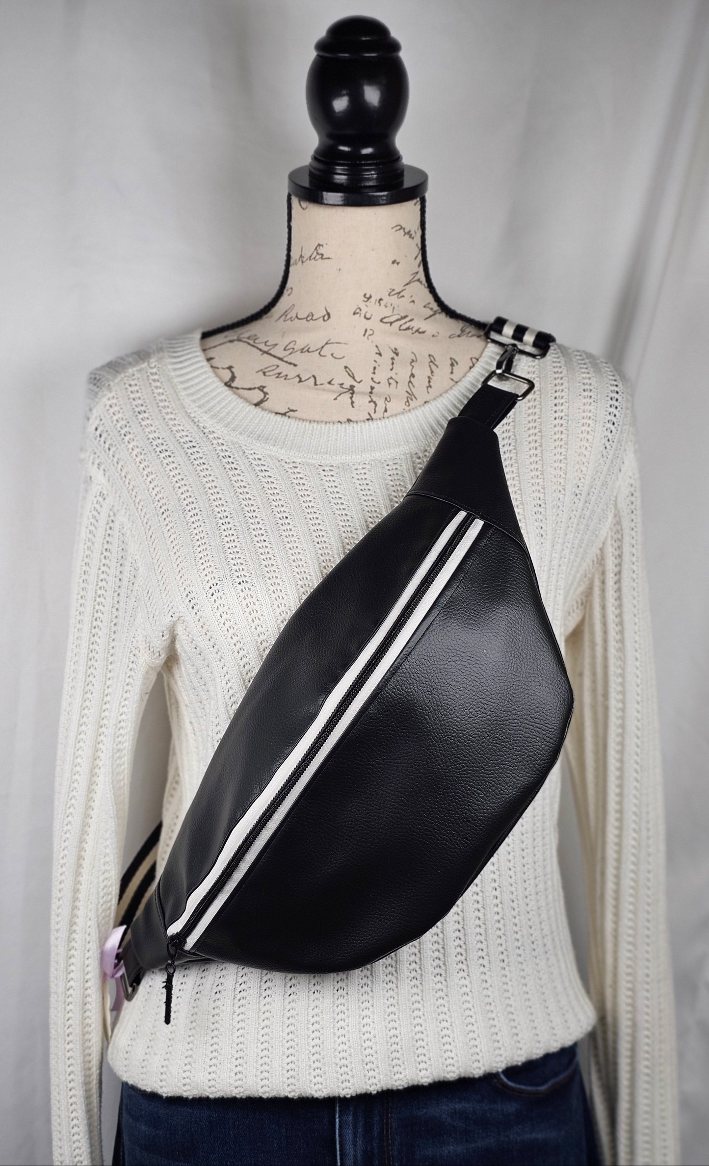 Black pebble faux leather sling, fanny pack with floral interior with one zipper pocket and one slip pocket. White zipper with "kindness" zipper pull and black and white striped strap.