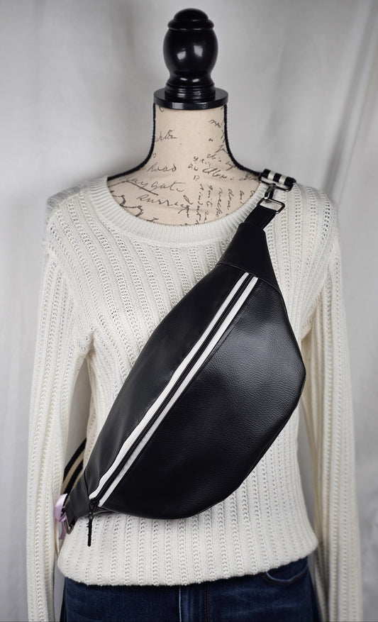 Black pebble faux leather sling, fanny pack with floral interior with one zipper pocket and one slip pocket. White zipper with "kindness" zipper pull and black and white striped strap.