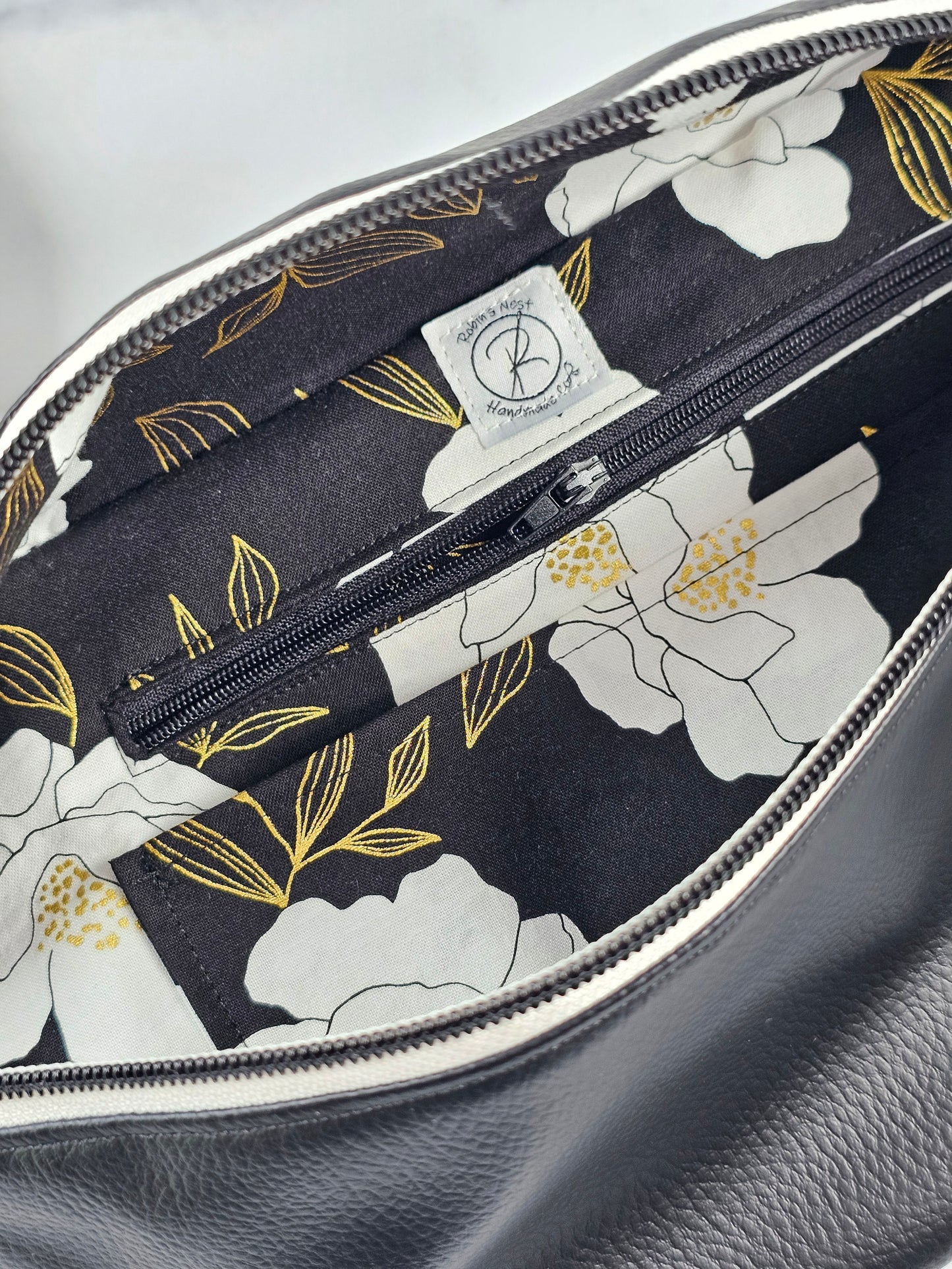 Black pebble faux leather sling, fanny pack with floral interior with one zipper pocket and one slip pocket. White zipper with "kindness" zipper pull and black and white striped strap.