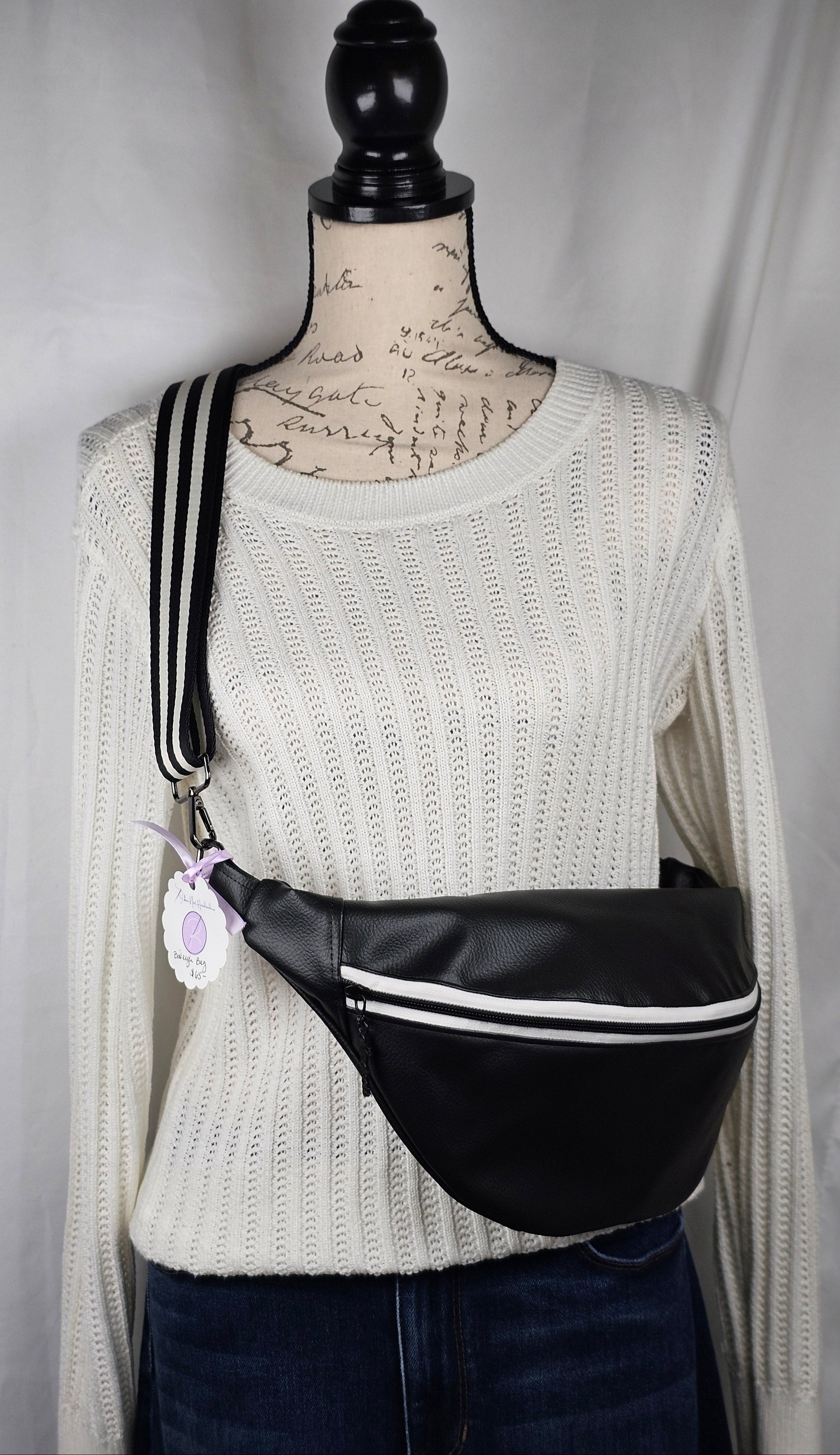 Black pebble faux leather sling, fanny pack with floral interior with one zipper pocket and one slip pocket. White zipper with "kindness" zipper pull and black and white striped strap.