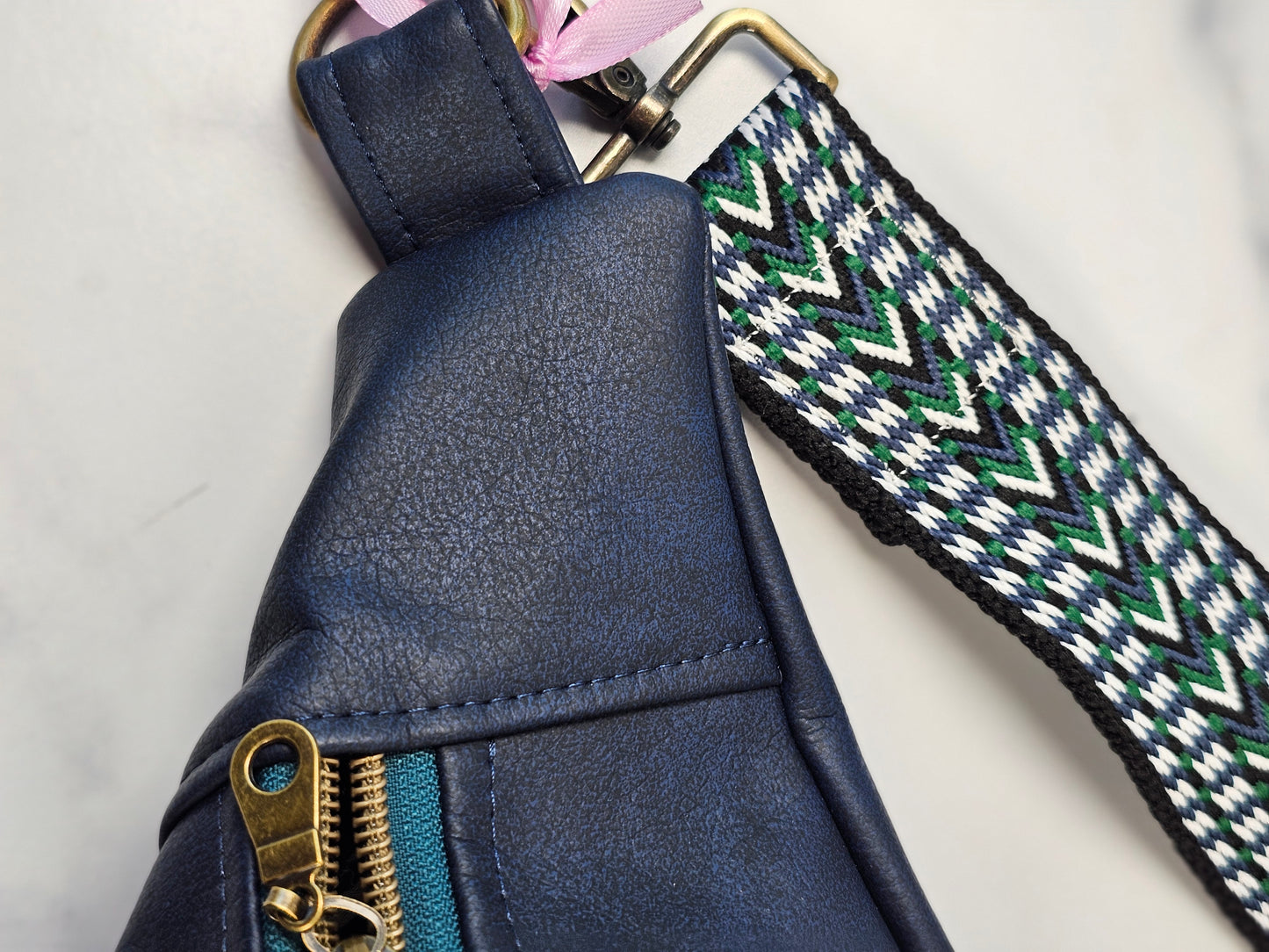 navy faux leather sling bag with multicolored strap and navy floral interior cotton lining with one zippered pocket and one slip pocket.