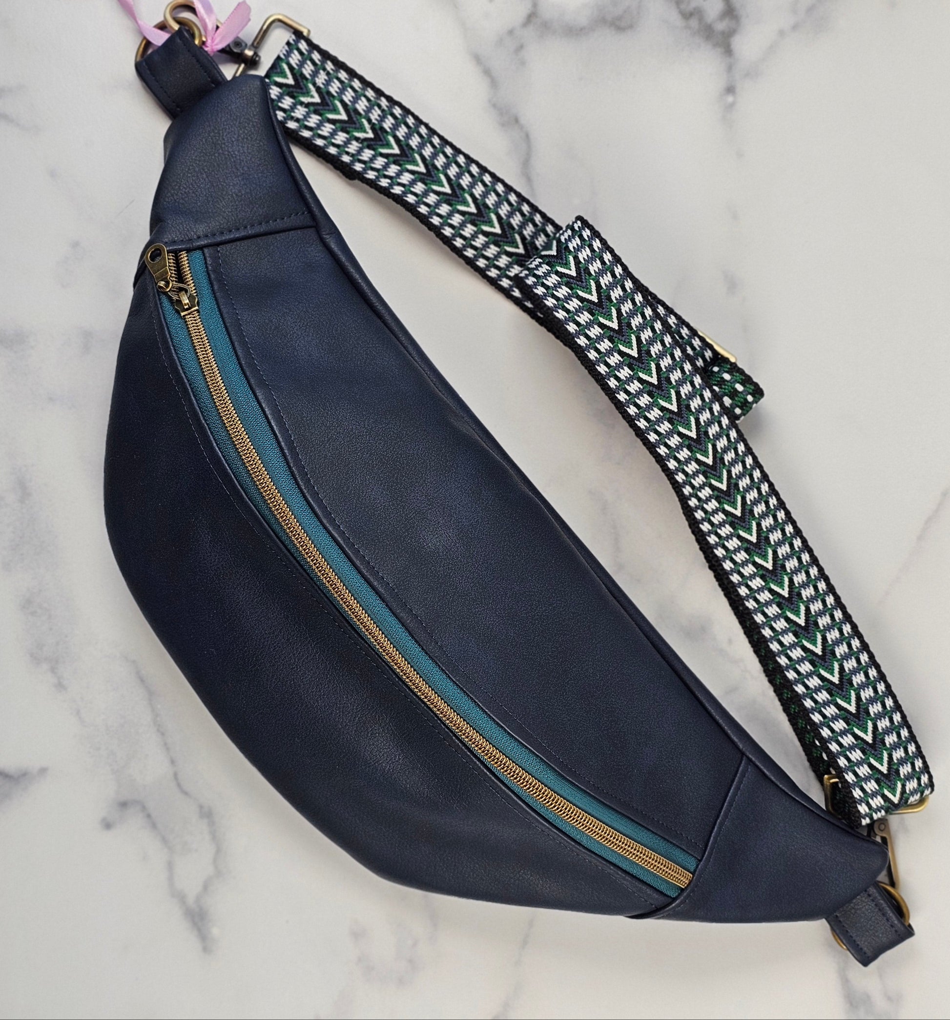 navy faux leather sling bag with multicolored strap and navy floral interior cotton lining with one zippered pocket and one slip pocket.