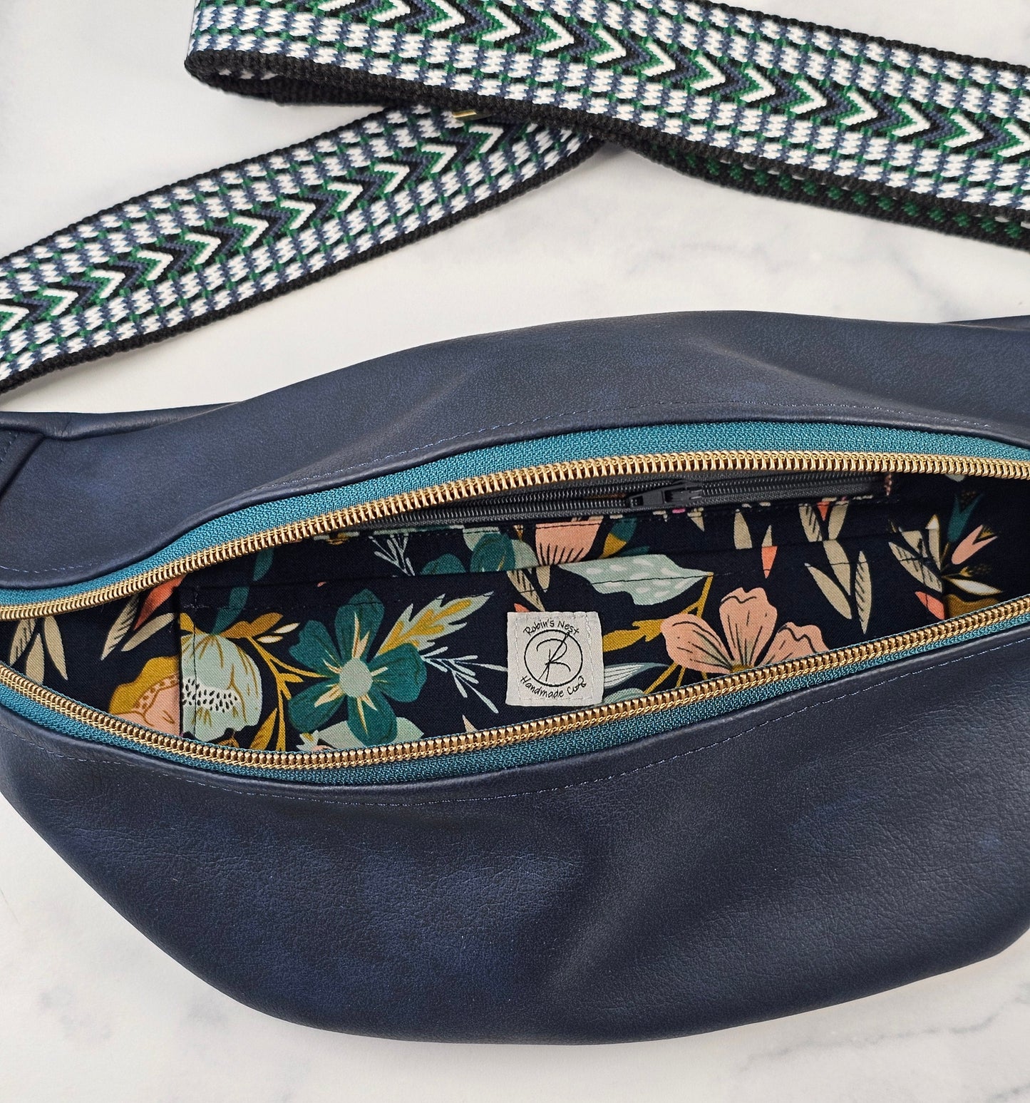 navy faux leather sling bag with multicolored strap and navy floral interior cotton lining with one zippered pocket and one slip pocket.