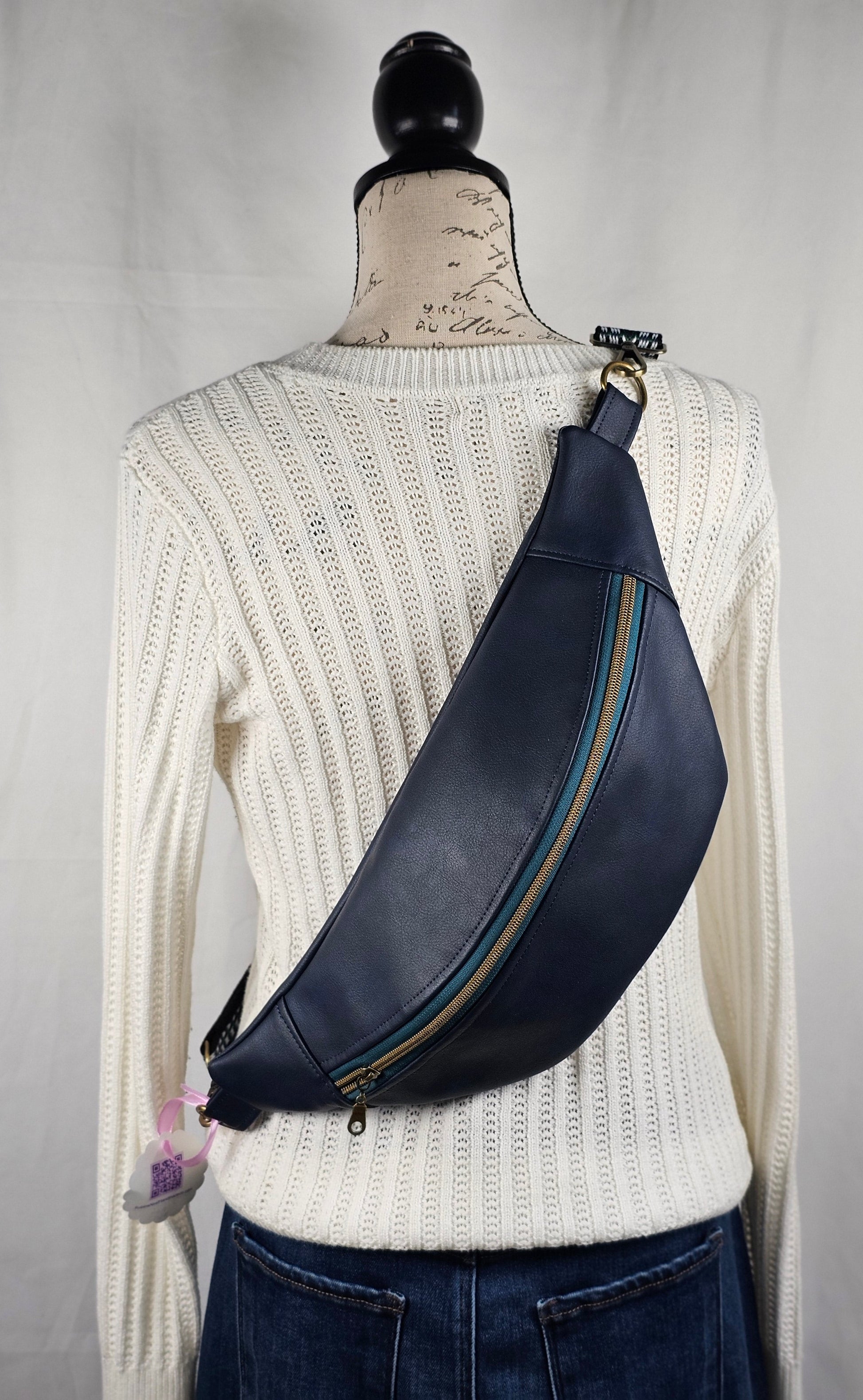 navy faux leather sling bag with multicolored strap and navy floral interior cotton lining with one zippered pocket and one slip pocket.