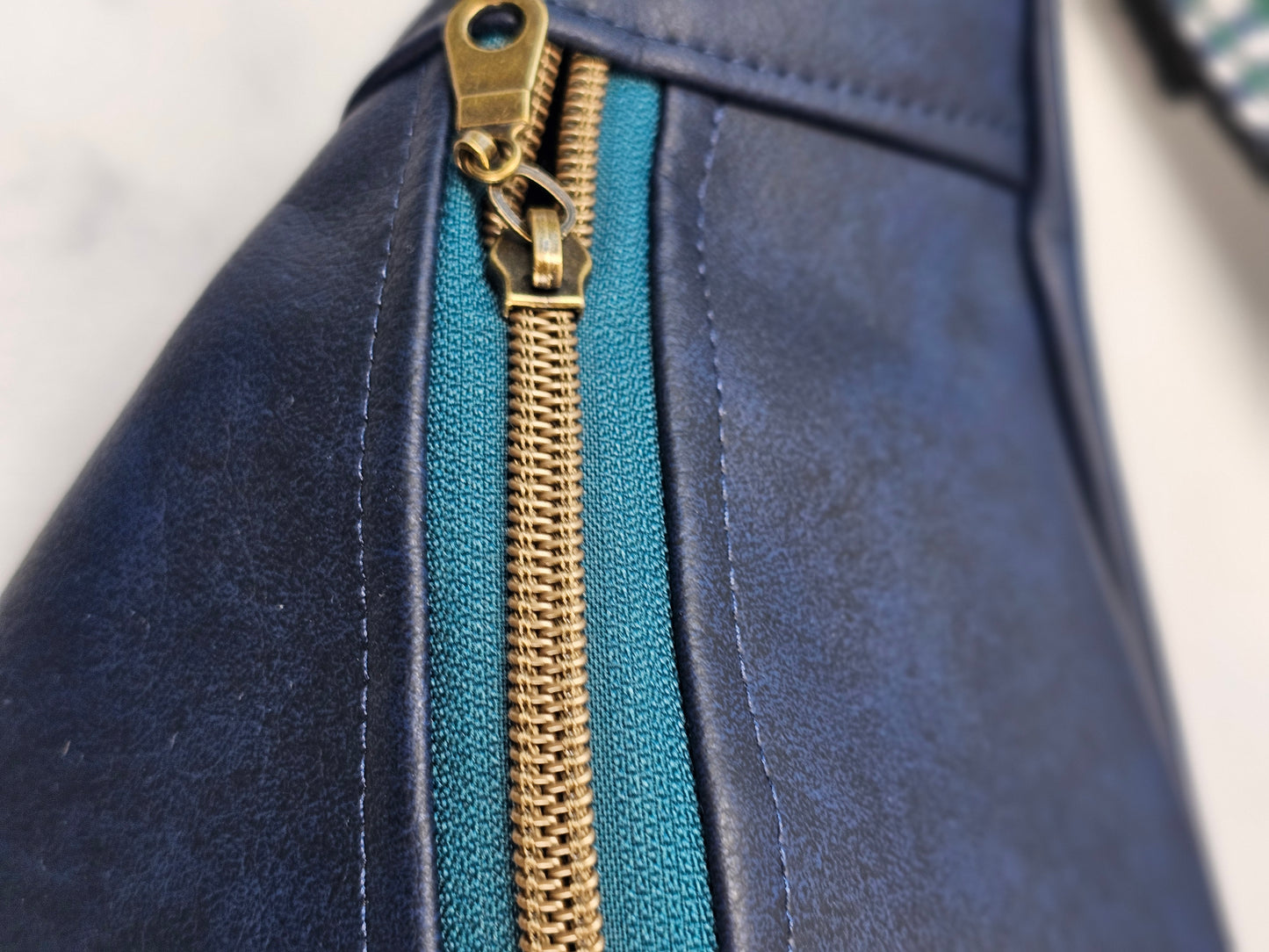 navy faux leather sling bag with multicolored strap and navy floral interior cotton lining with one zippered pocket and one slip pocket.