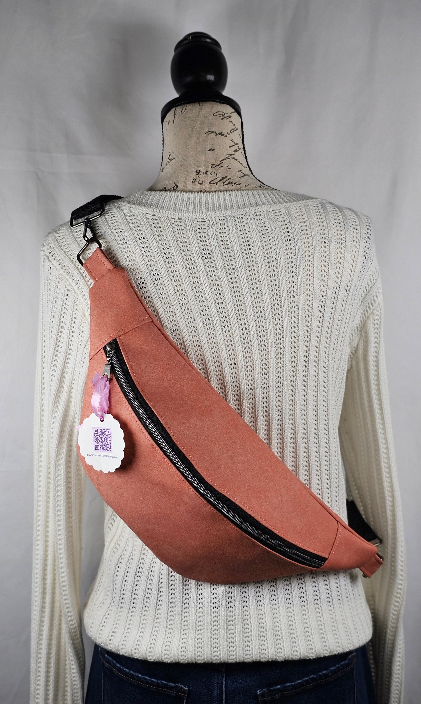 pink sling bag with black accents with a visible brand label on a mannequin against a gray background