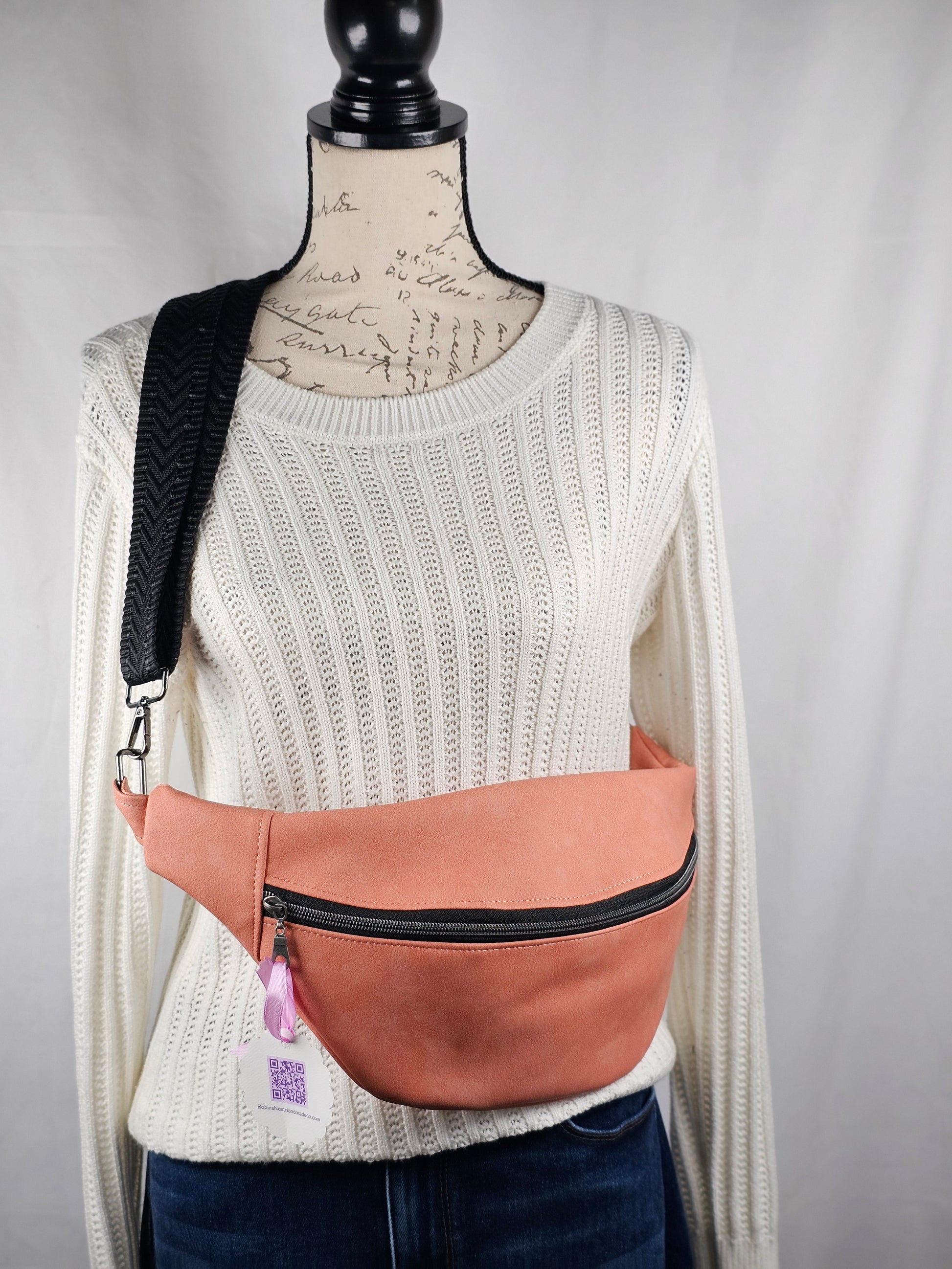Person wearing a white sweater with a pink faux leather bag over their shoulder on a gray background