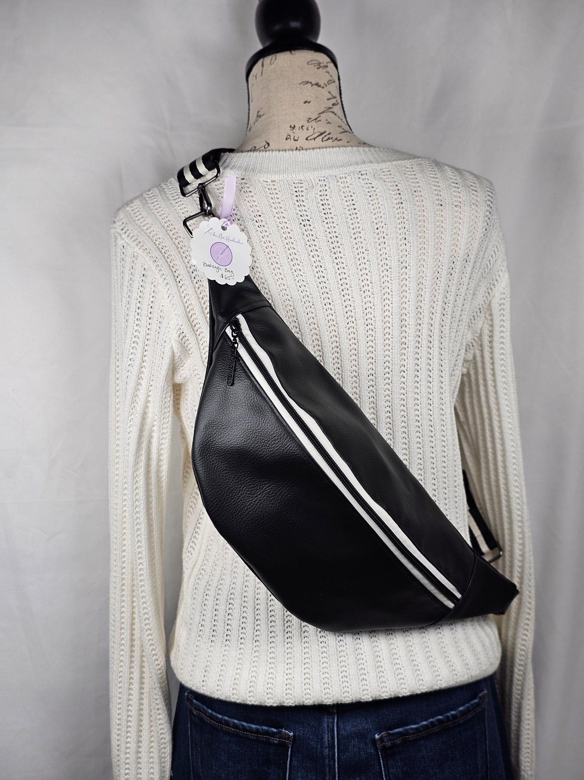 Black pebble faux leather sling, fanny pack with floral interior with one zipper pocket and one slip pocket. White zipper with "kindness" zipper pull and black and white striped strap.