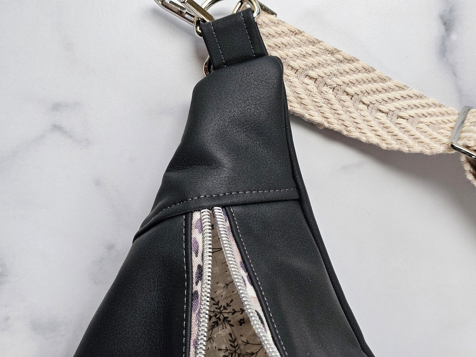 Dark gray faux leather sling fanny pack with gray leopard print zipper and light gray chevron strap. Interior gray floral with interior zip and slip pockets.